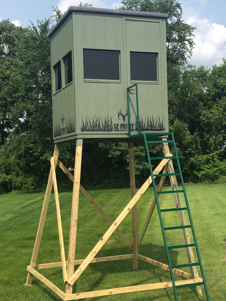 6x6_Hunting_Blind_The_Double_Barrel_with_Optional_10_Stand_1024x1024 - Ideal Land Management | Forestry mowing & mulching, food plots, hunting blinds Elevated green hunting blind on a wooden stilt frame with a ladder, overlooking a grassy field.