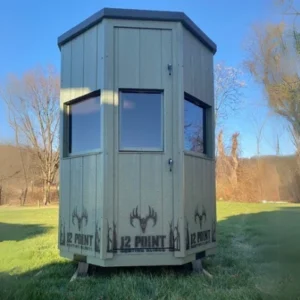 Small gray wooden observation tower on a grassy lawn, with three windows and '12 POINT' logos at the base, in a park.