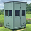 booner - Ideal Land Management | Forestry mowing & mulching, food plots, hunting blinds Green wooden hunting blind with multiple small windows and a centered door, branded '12 Point', placed on a grassy field near a pond.